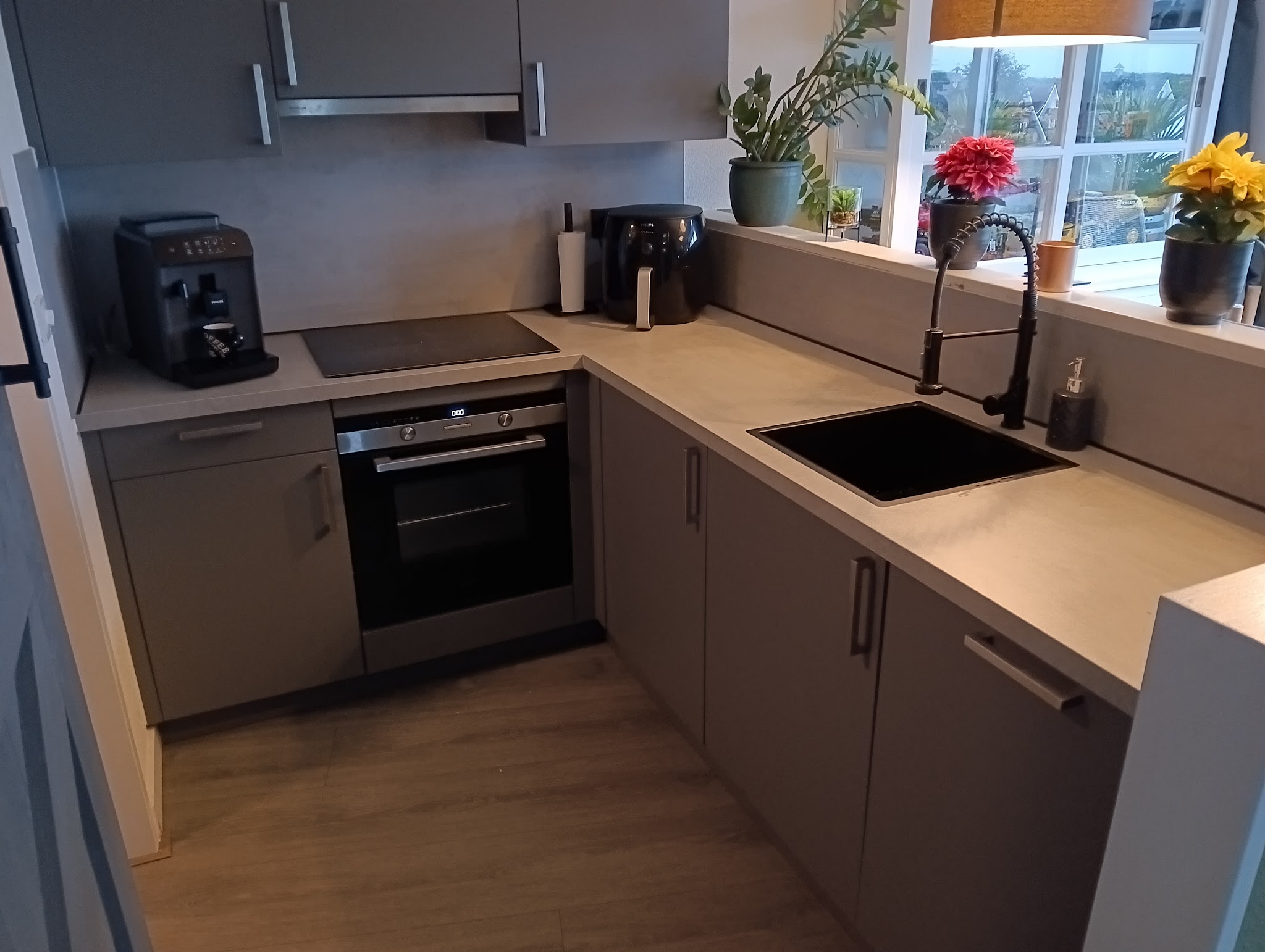 Opgeleverde keuken met grijze fronten, zwarte spoelbak en inductiekookplaat