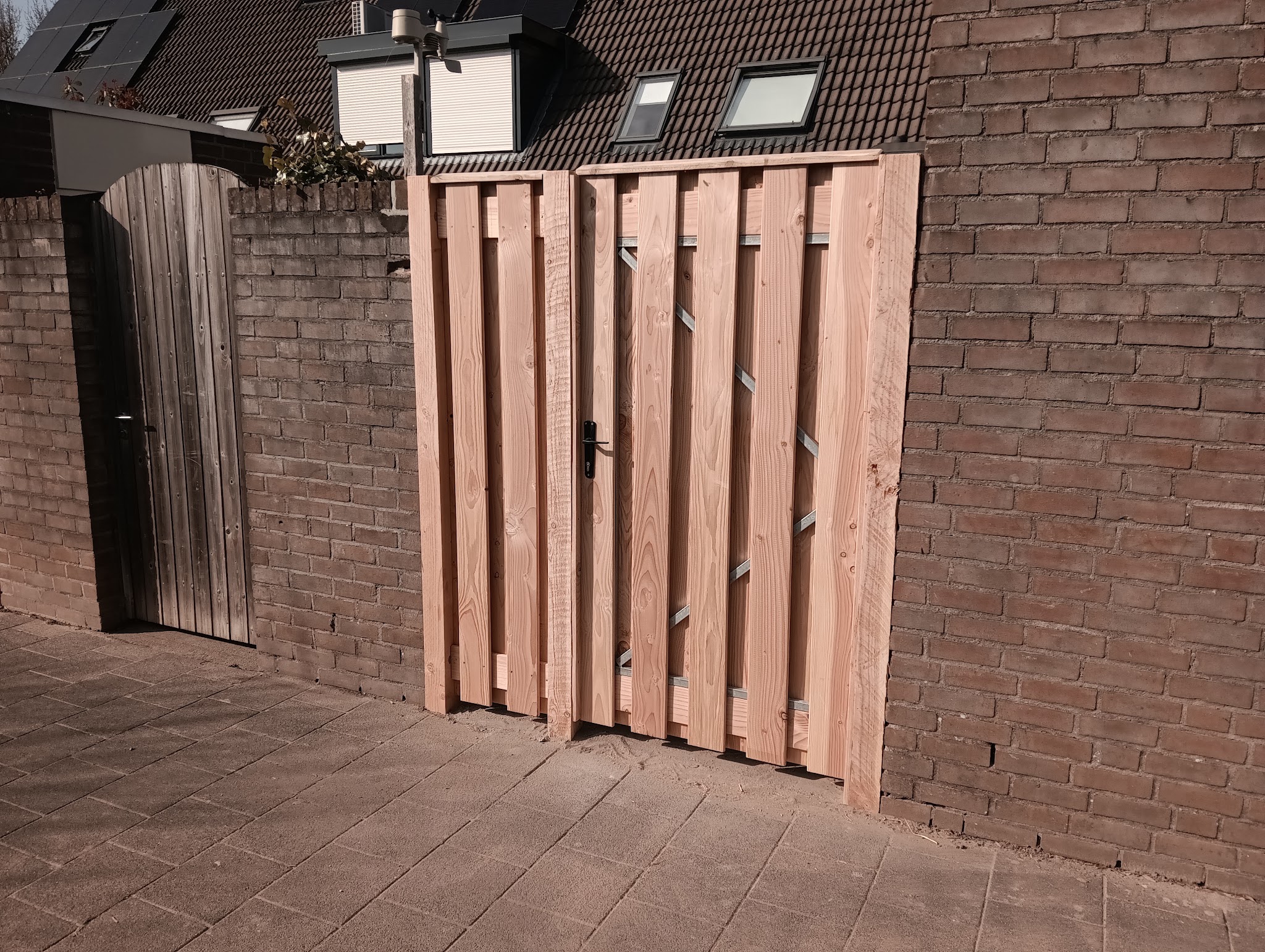 Nieuwe houten tuinpoort in een bakstenen tuinmuur